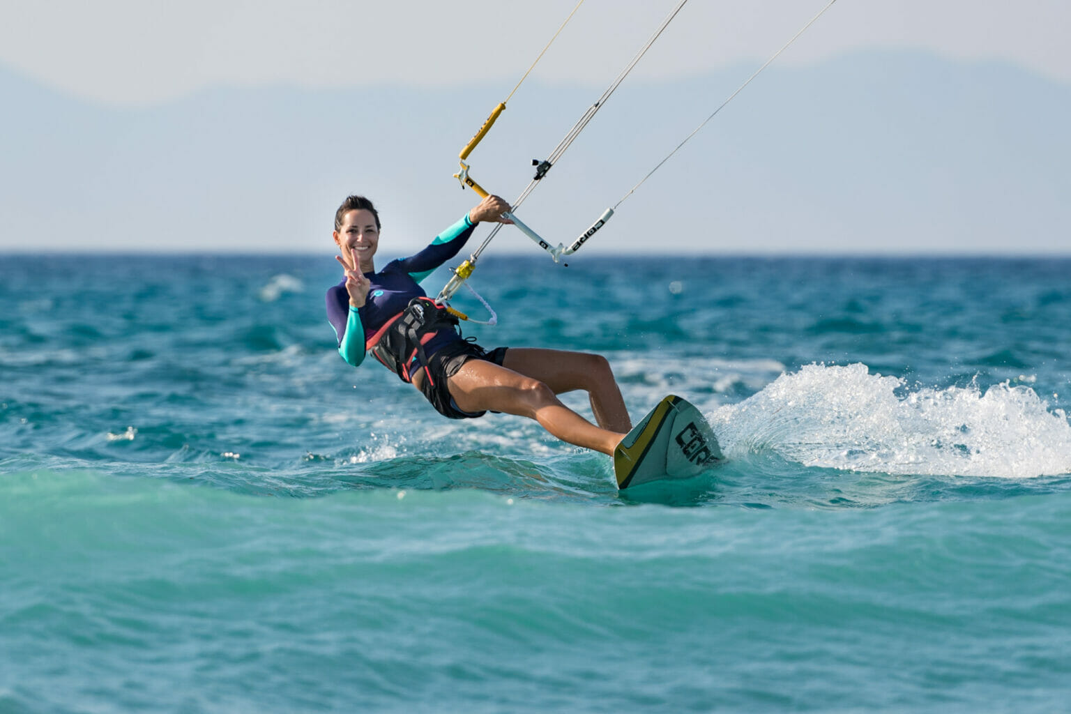 Frau zeigt Peace-Zeichen beim Kitesurfen auf dem offenen Meer