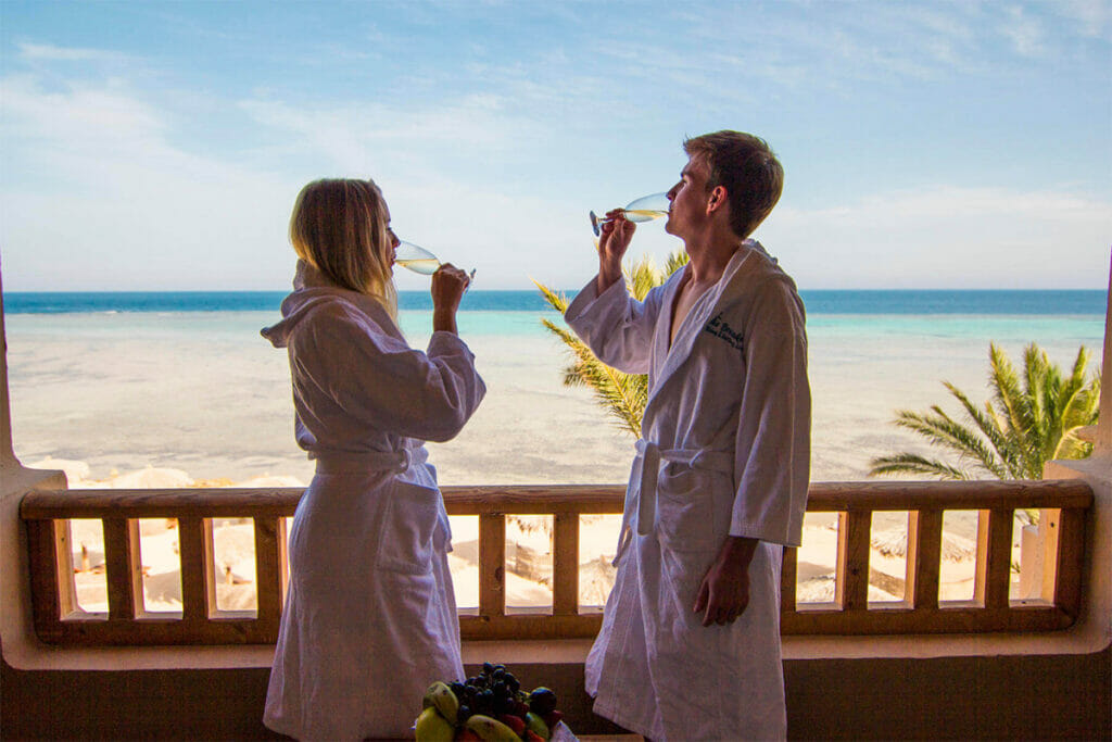 Pärchen trinkt Sekt am Balkon eines Hotels mit Blick auf Strand und Meer