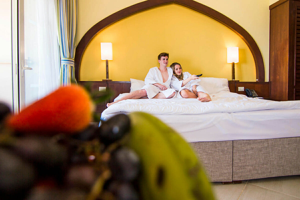 Couple watching TV in bathrobe on bed in hotel room